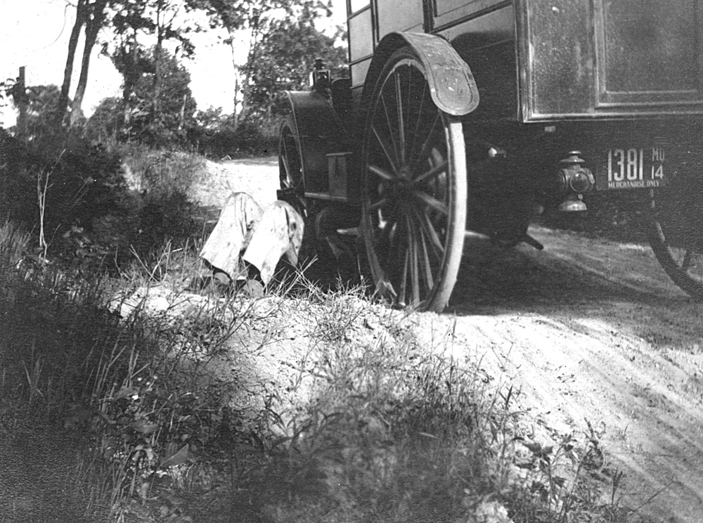 1800s circa car with man under car working on a dirt road